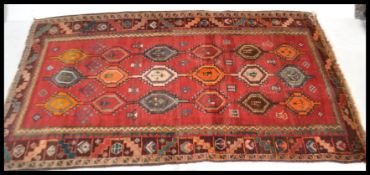 A 20th Century Kazak style rug having a red ground with geometric borders and a diamond patterned