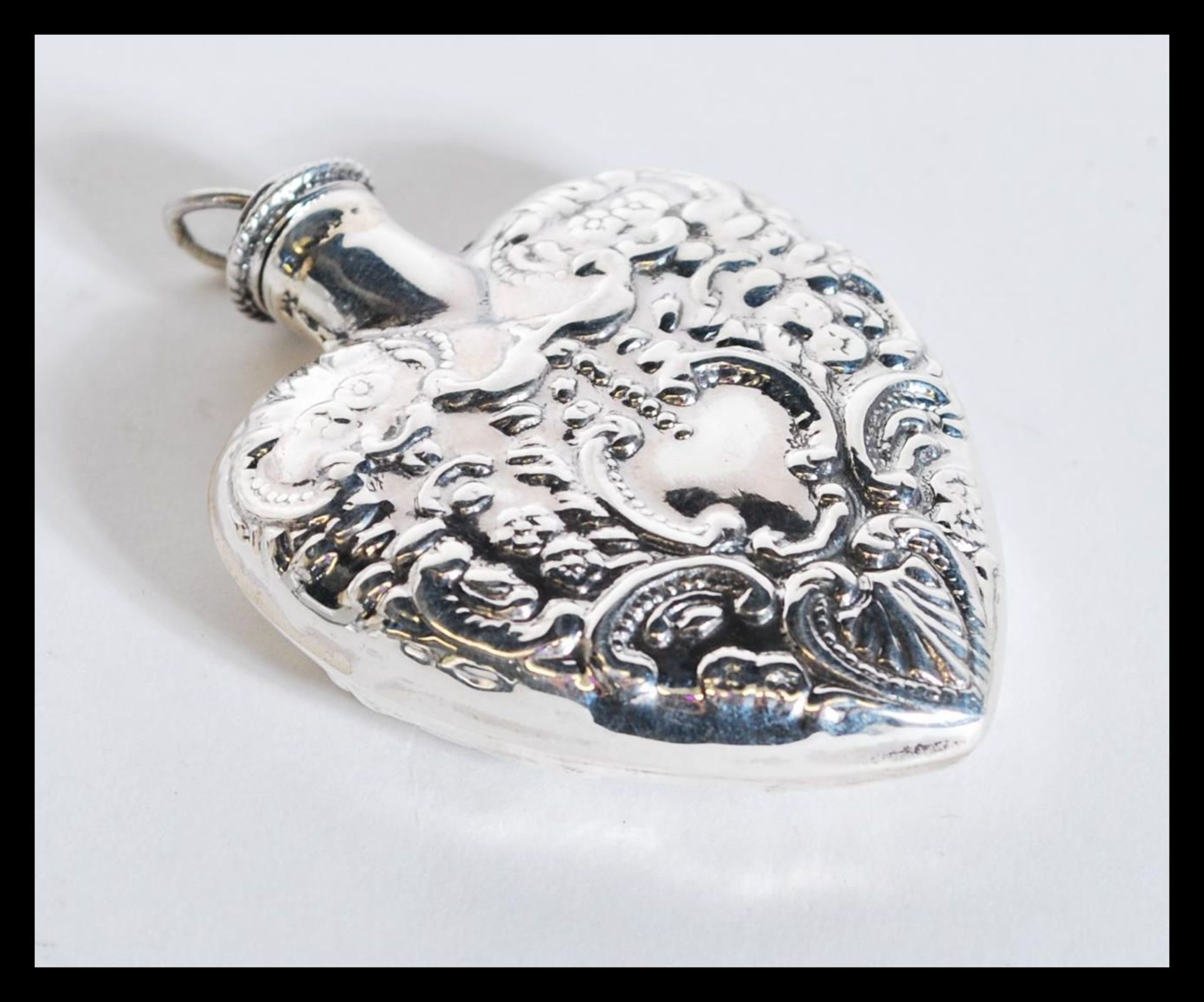 A sterling silver perfume bottle in the form of a heart having scrolled decoration. Weighs 21 grams.