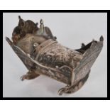 A silver miniature doll's house crib having embossed decoration to the sides and rockers to the