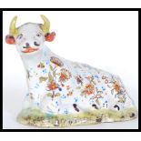 A 19th Century Delft Faience Staffordshire type figurine in the form of a seated reclined cow with