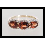 A hallmarked 9ct gold diamond and orange stone ring having three faceted stones with halos of