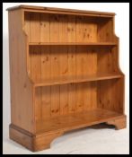 An antique style country pine waterfall bookcase cabinet raised on bracket feet with a graduating
