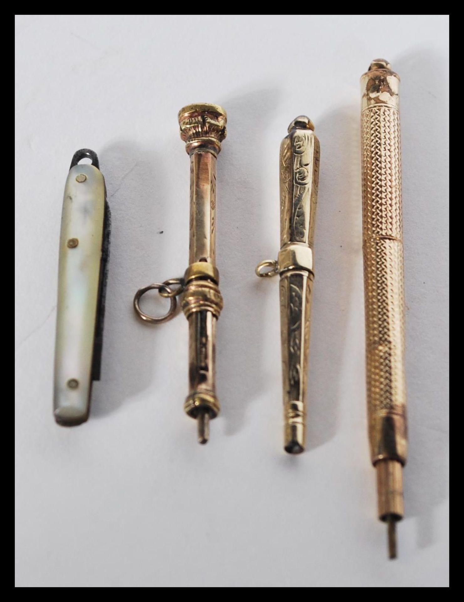 A group of three yellow metal propelling pencils along with a miniature mother of pearl pen fruit