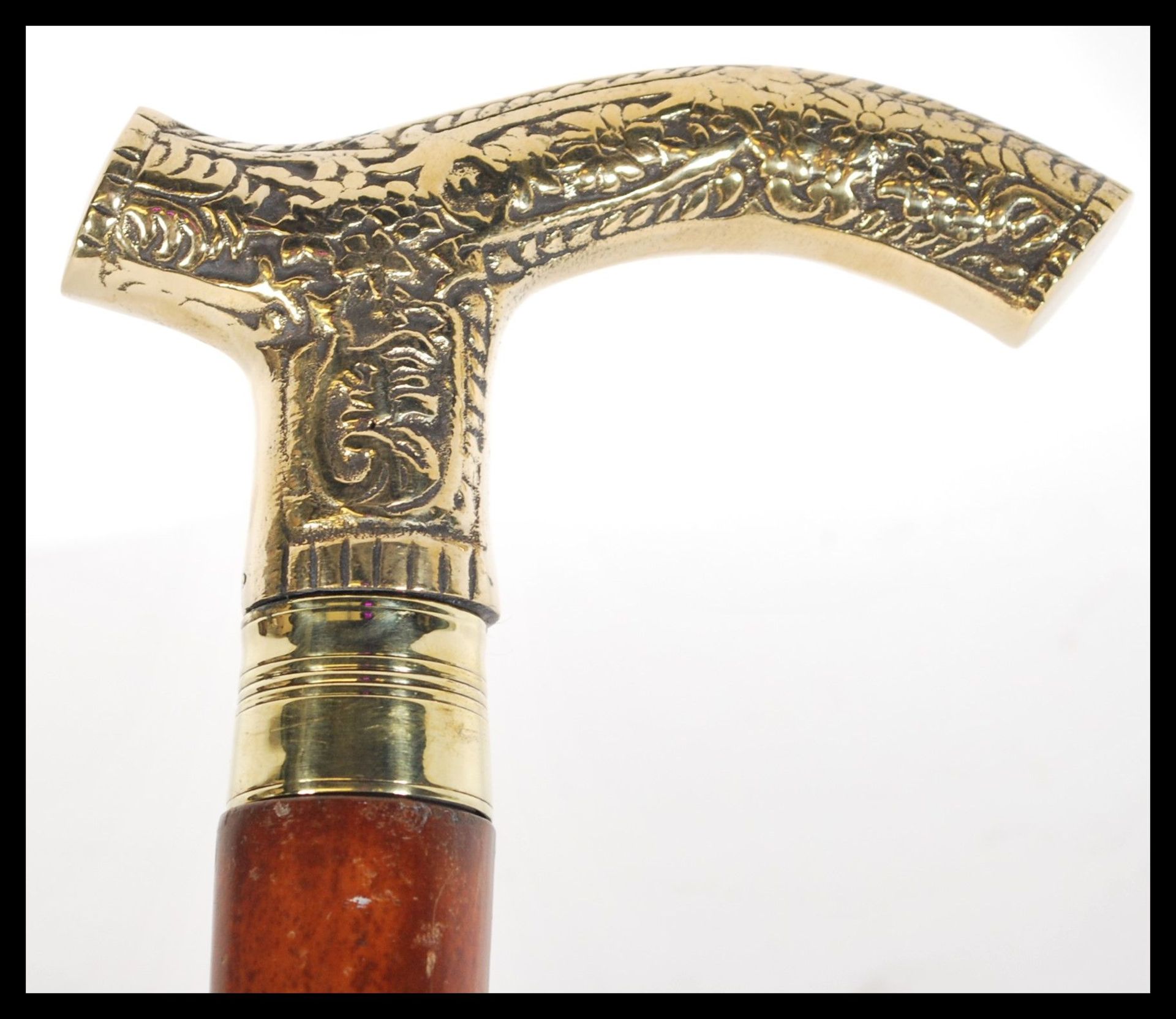 A malacca walking stick having a brass hooked handle having embossed floral detailing. Measures