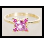 A hallmarked 18ct gold ring set with a brilliant cut pink sapphire and four small accent stones.