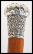 A wooden walking stick cane having a silver hallmarked top with scrolled decoration. Hallmarked