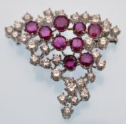 An 18ct white gold ruby and diamond brooch pin. The brooch having stylised scattered festoon of