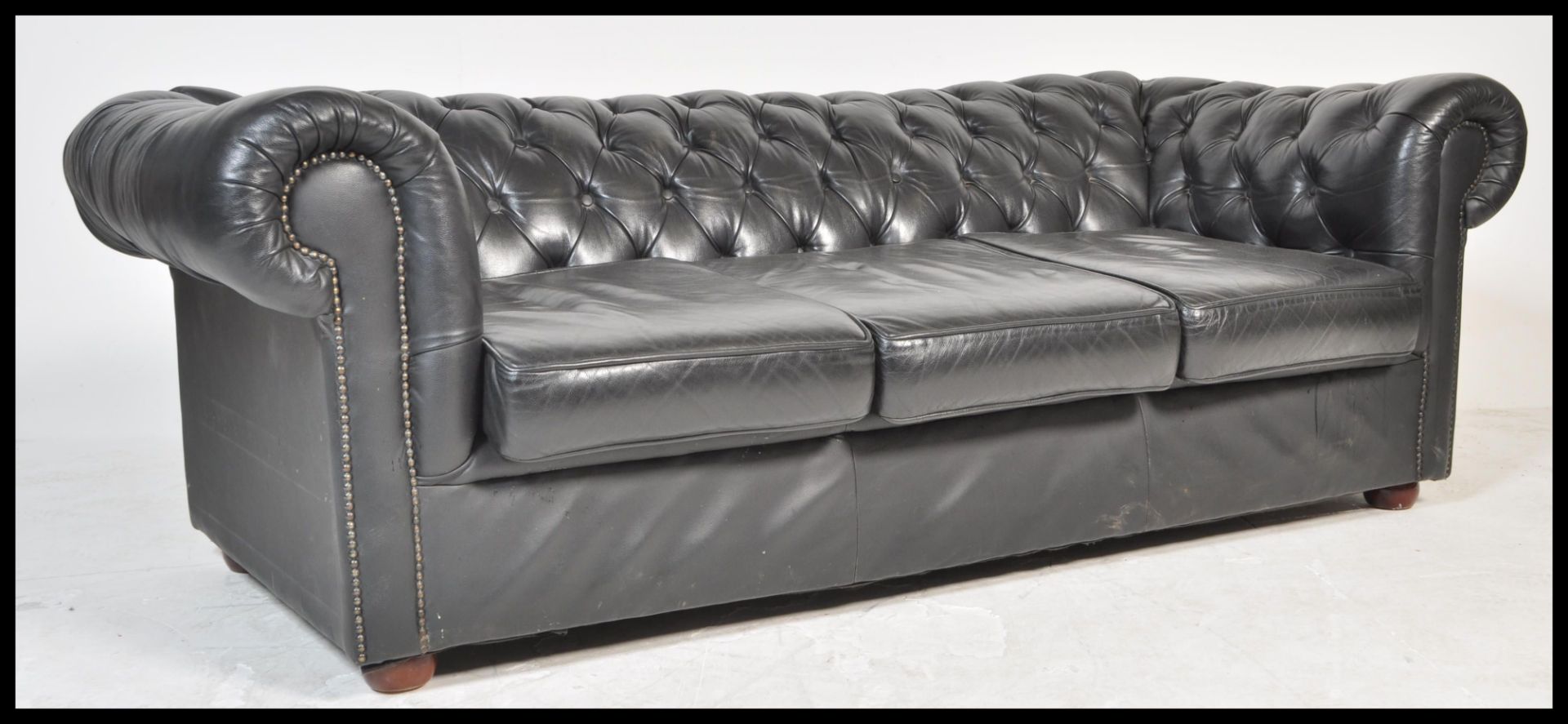 A contemporary black leather button back three seater Chesterfield sofa with button back and
