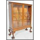 A 1930's mahogany Queen Anne revival china display cabinet being raised on claw and ball feet with