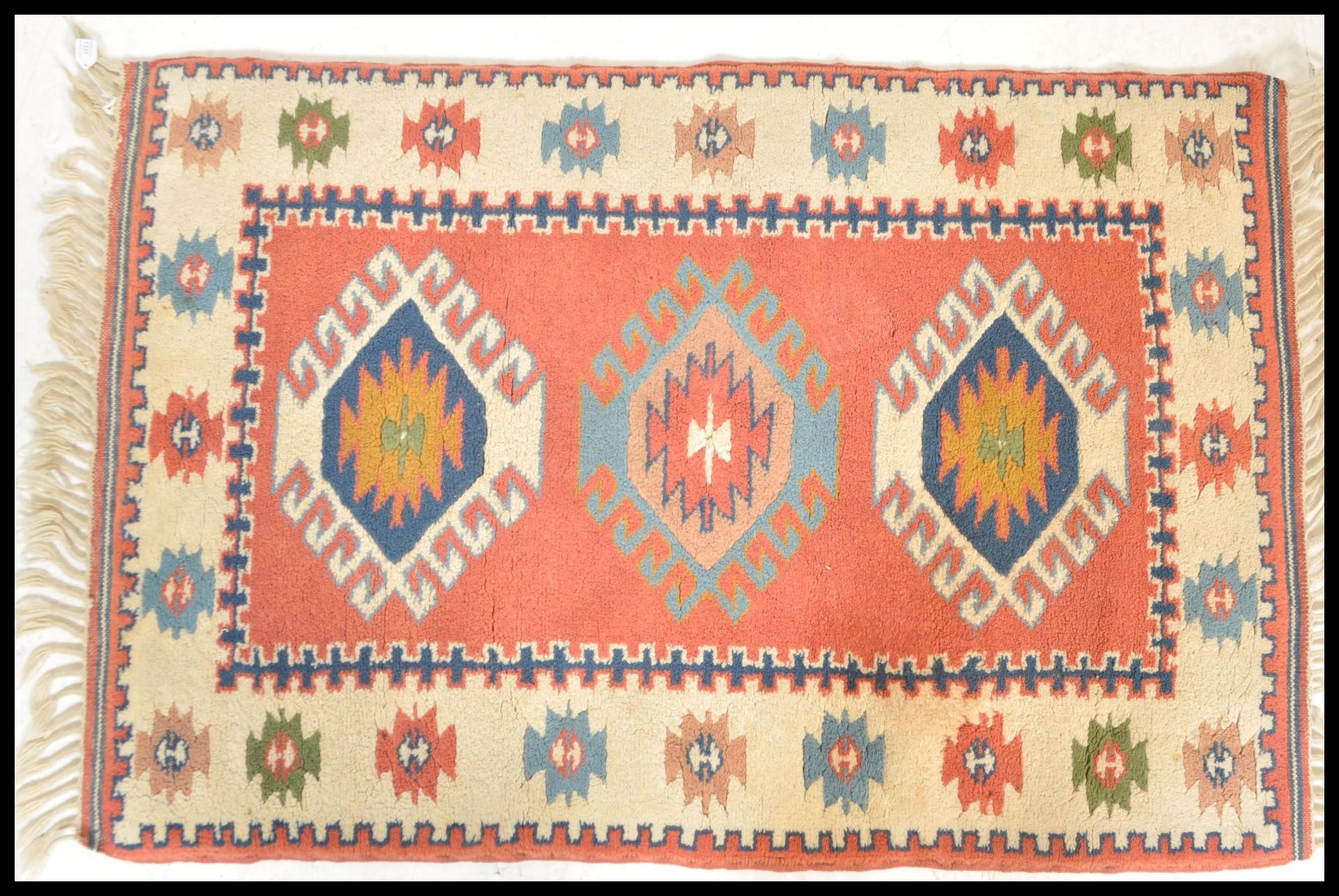 A 20th Century woven tribal carpet rug having a cream ground with a central red panel with three