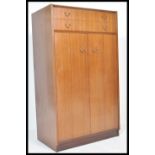 A mid century Ernest Gomme tola / teak wood bachelors wardrobe of small proportions being raised