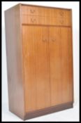 A mid century Ernest Gomme tola / teak wood bachelors wardrobe of small proportions being raised