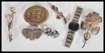 A collection of silver brooches and a silver watch. The brooches include a swan brooch, a double