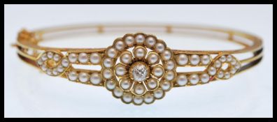 A 19th Century Victorian gold and pearl hinged bangle bracelet set with a central old cut diamond