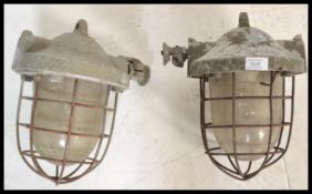 A pair of retro 20th Century industrial factory bulk cage lights, having a cast iron body, glass