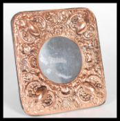 A copper easel back photograph picture frame of square form having rococo decoration.