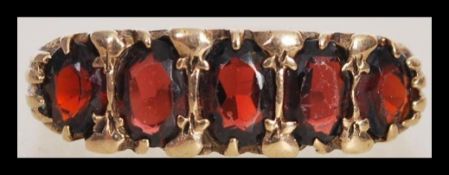 A stamped 375 9ct gold ring set with five red stones within a decorative scrolled setting. Total