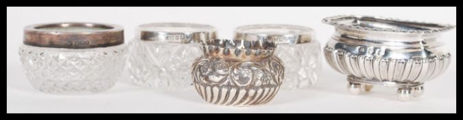 A group of silver hallmarked and cut glass table salts to include a half reeded and foliate scroll