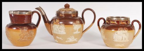 A Doulton Lambeth three piece silver mounted stoneware glazed tea service consisting of teapot, twin