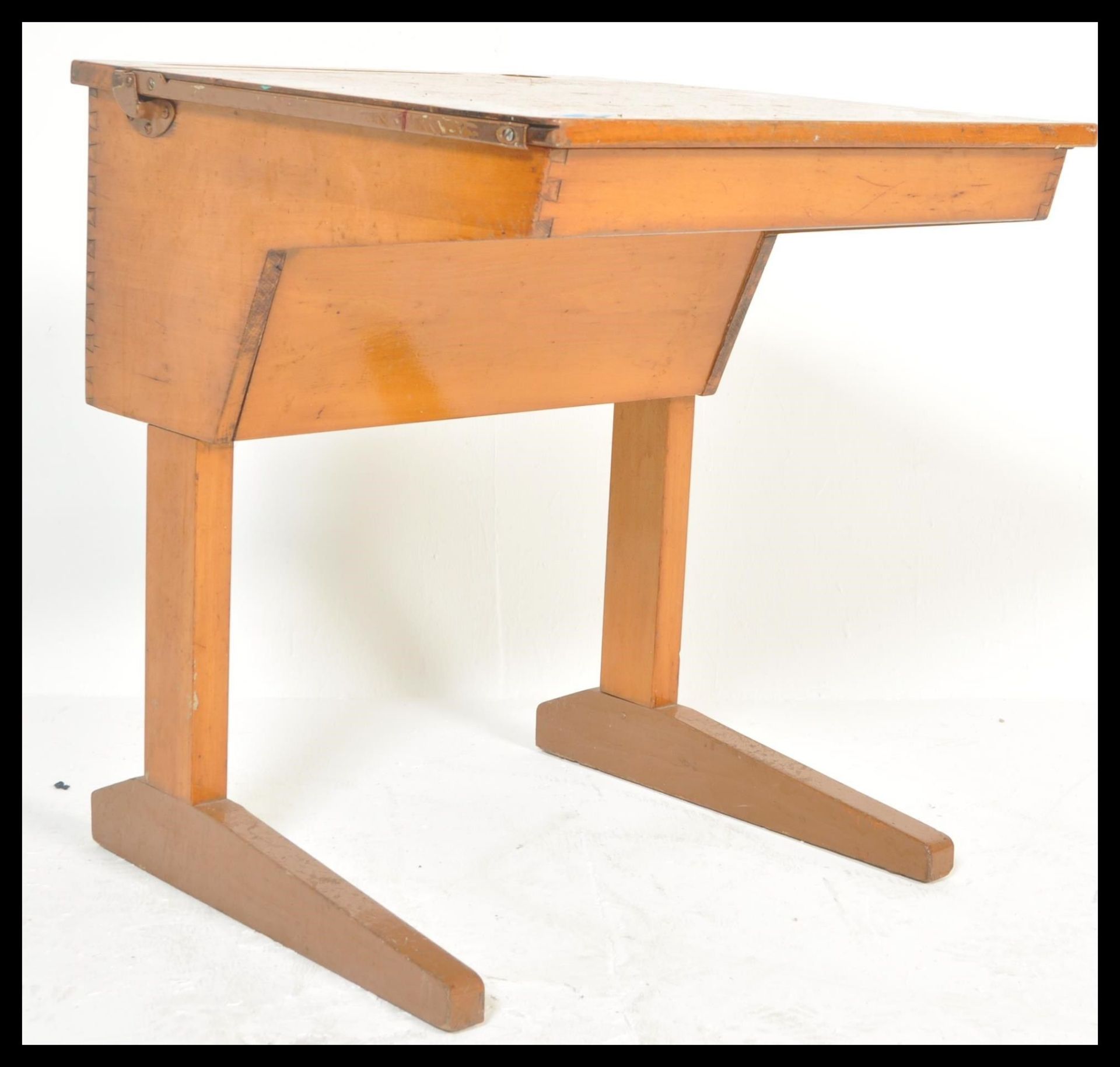 A late Victorian beech wood childs school desk being raised on shaped leg supports with sloped