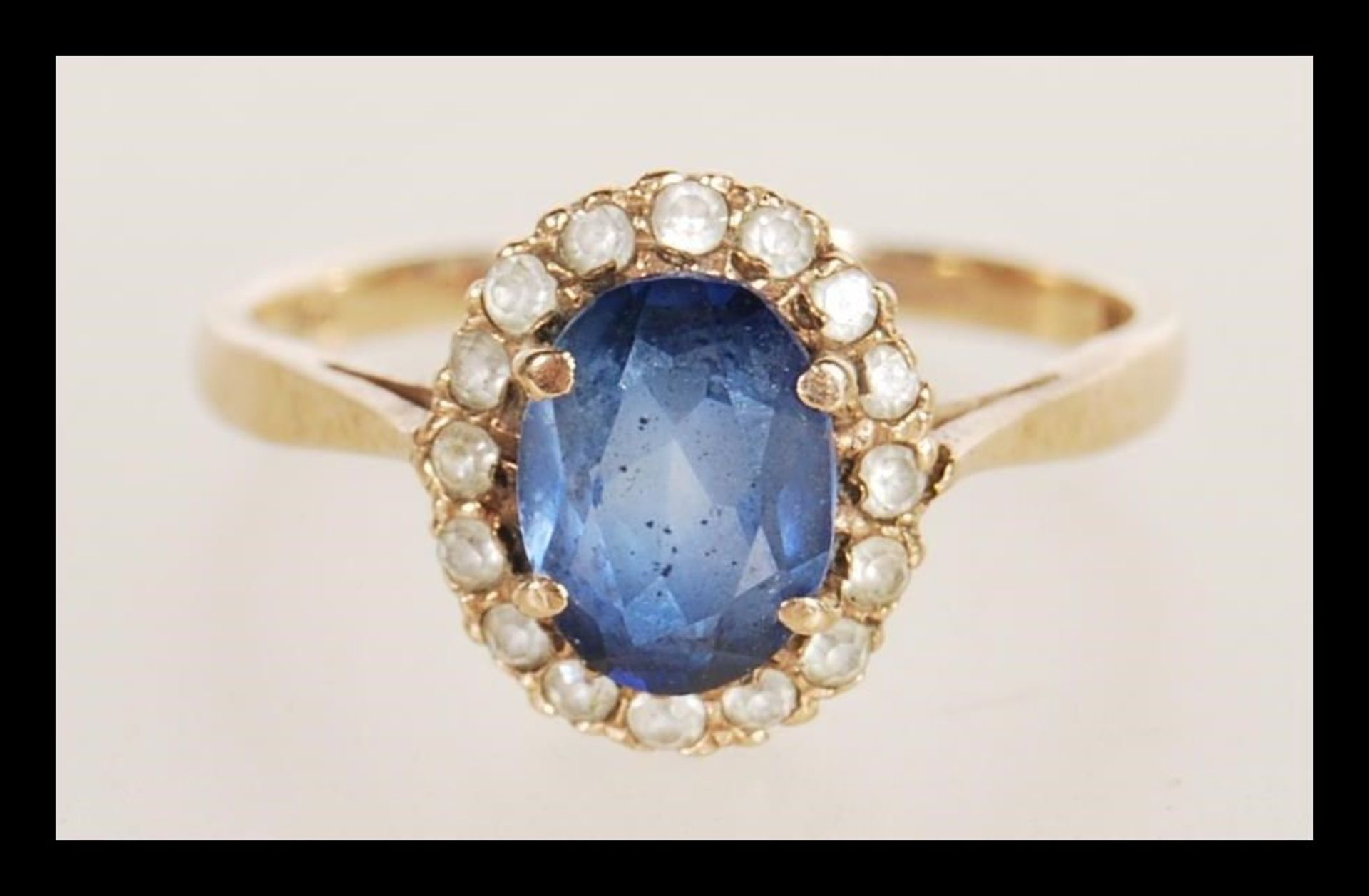 A hallmarked 9ct gold ring prong set with an oval cut synthetic sapphire set with a halo of white