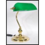 A vintage 20th century bankers desk lamp having an adjustable green glass shade raised on a brass