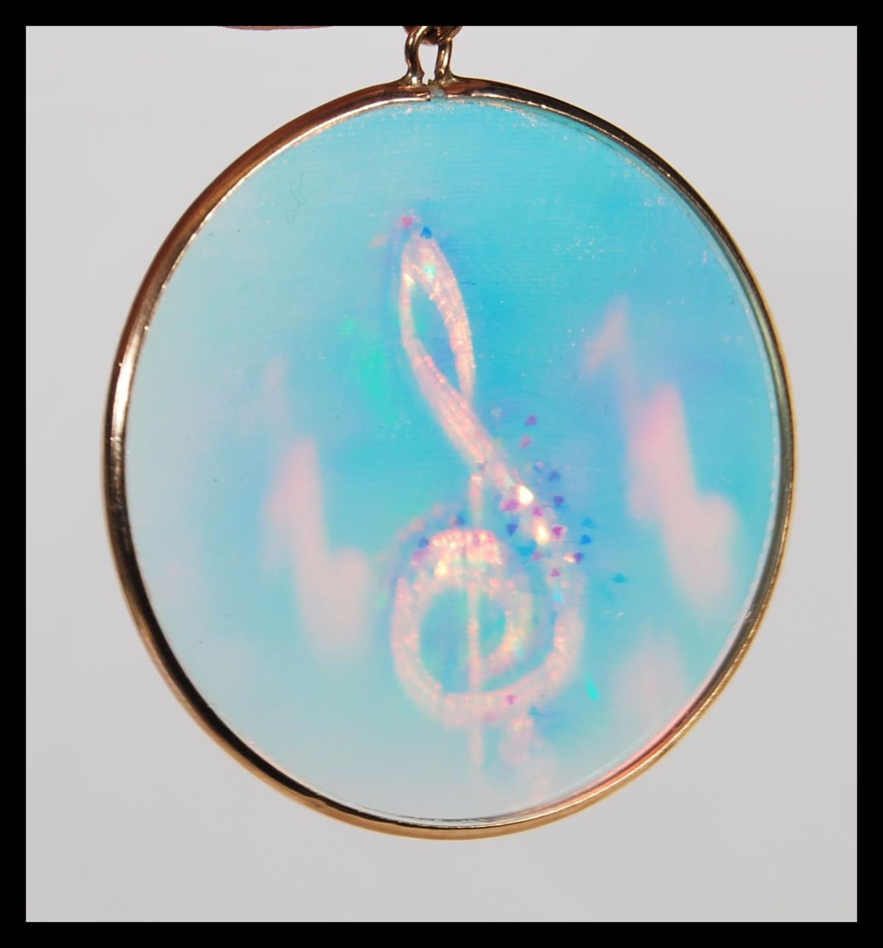 A 9ct gold roundel pendant inset with hologram of musical notes together with a 9ct chain.  The