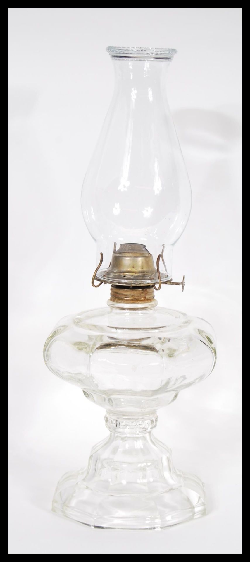 An late 19th / early 20th Century oil lamp having a clear glass and brass fittings with a flu