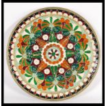 A 20th Century brass wall charger plate with enamelled geometric detailing in red and green hues.