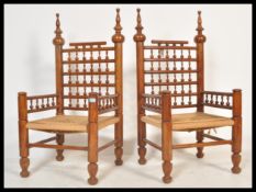 A pair of 20th Century Moroccan hardwood carver armchairs having rush seat pads raised on turned