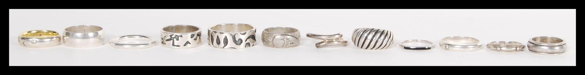 A group of 12 sterling silver band rings to include white stone set example, cross over ring,