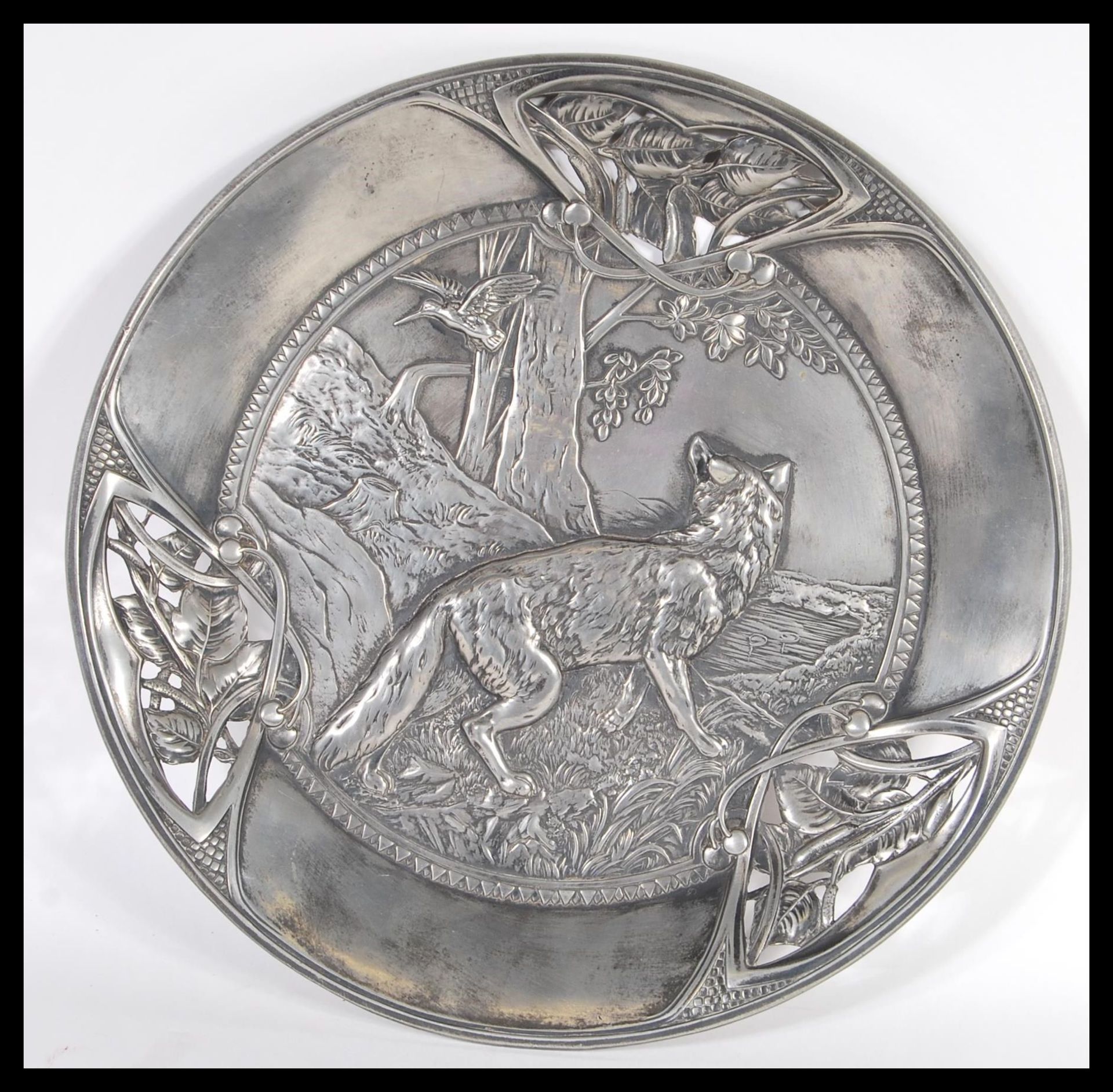 A 20th Century pewter wall charger having a raised scene of a fox in woodland with a bird flying