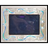 A 20th Century Tiffany style easel back photo frame having a silver frame with enamelled Art Nouveau