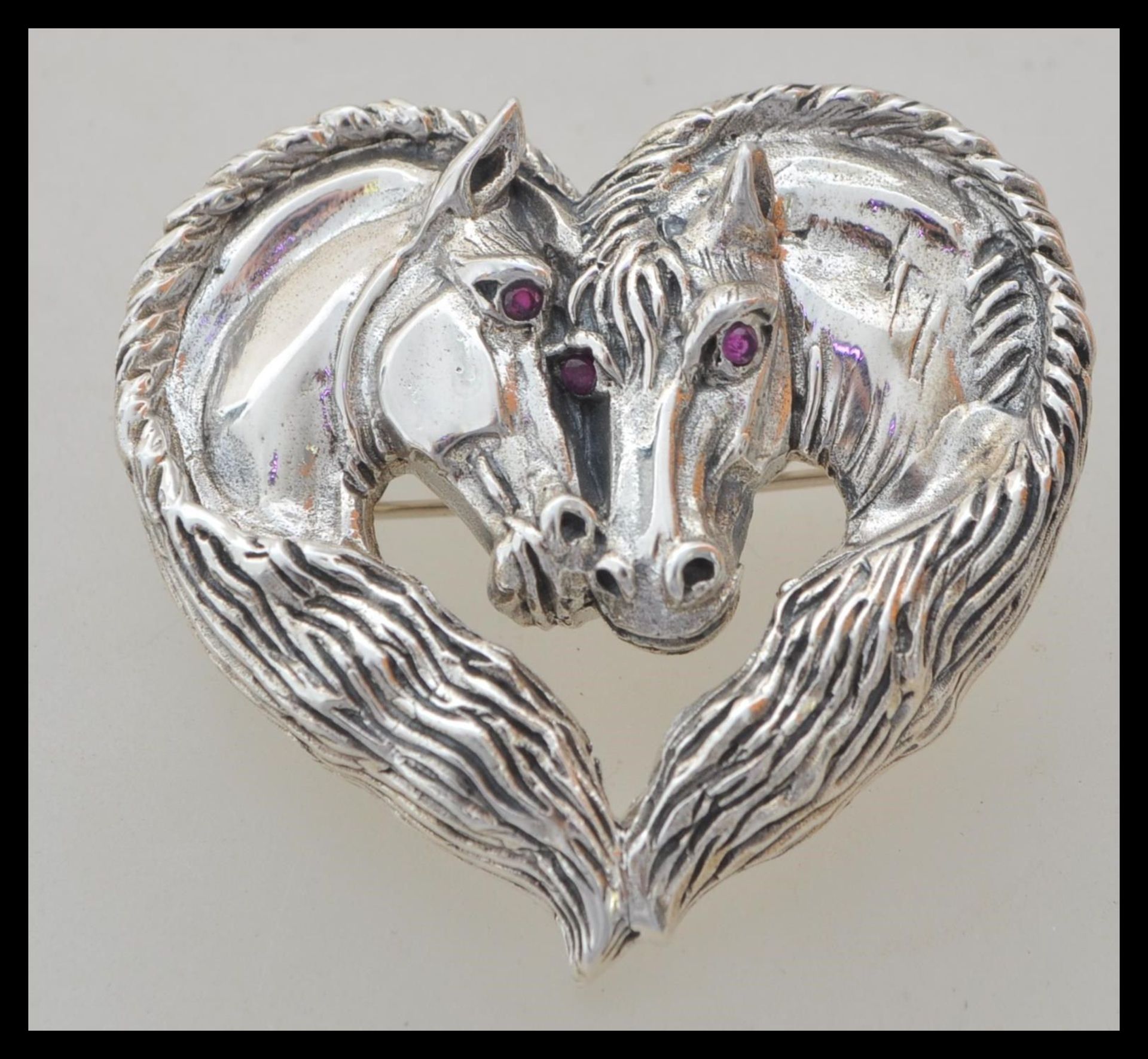 A stamped 925 silver heart brooch in the form of two horses having red stone eyes. Weight 19.1g.