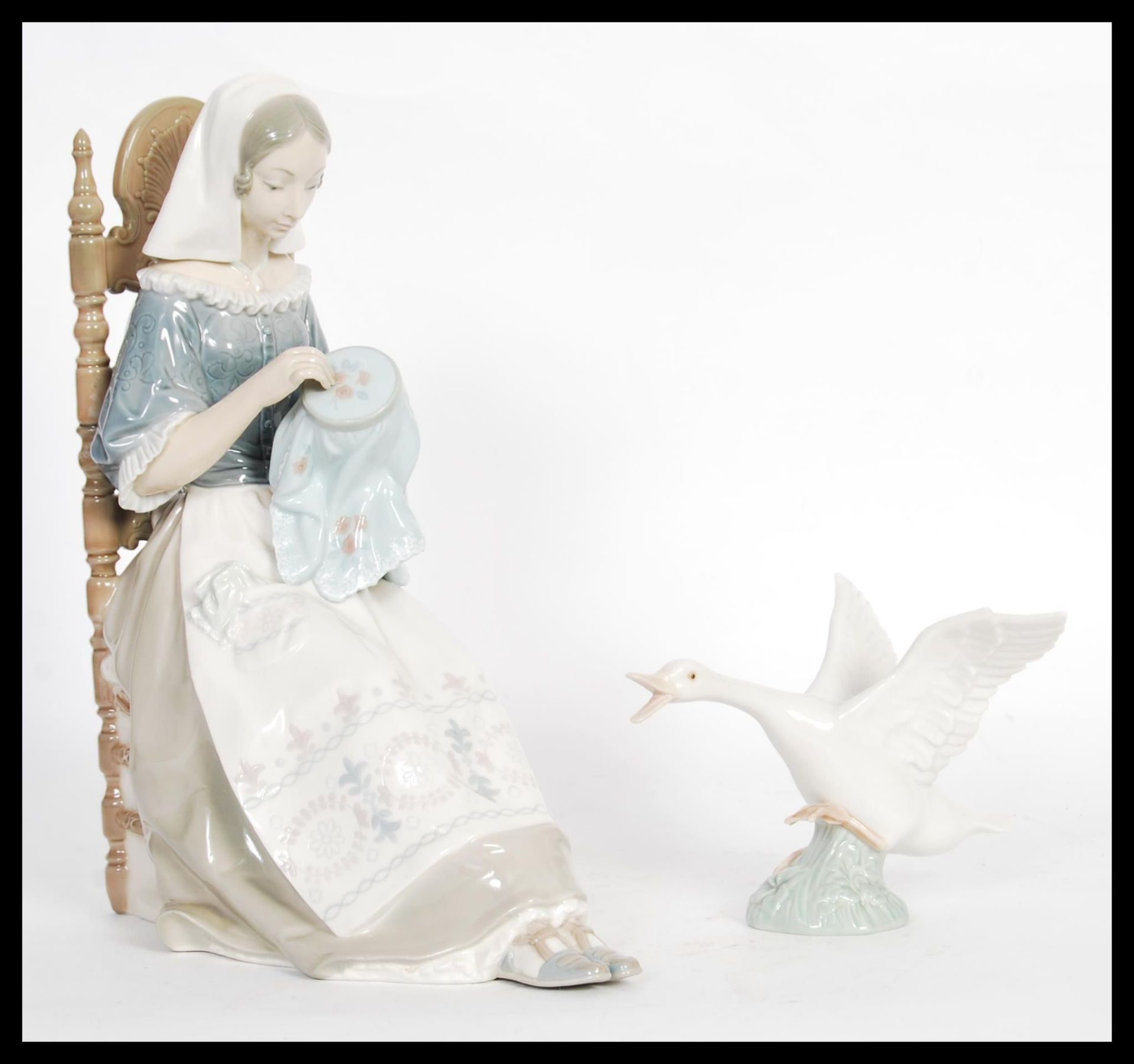 A Lladro porcelain figure depicting a woman doing embroidery seated in a chair along with a figurine