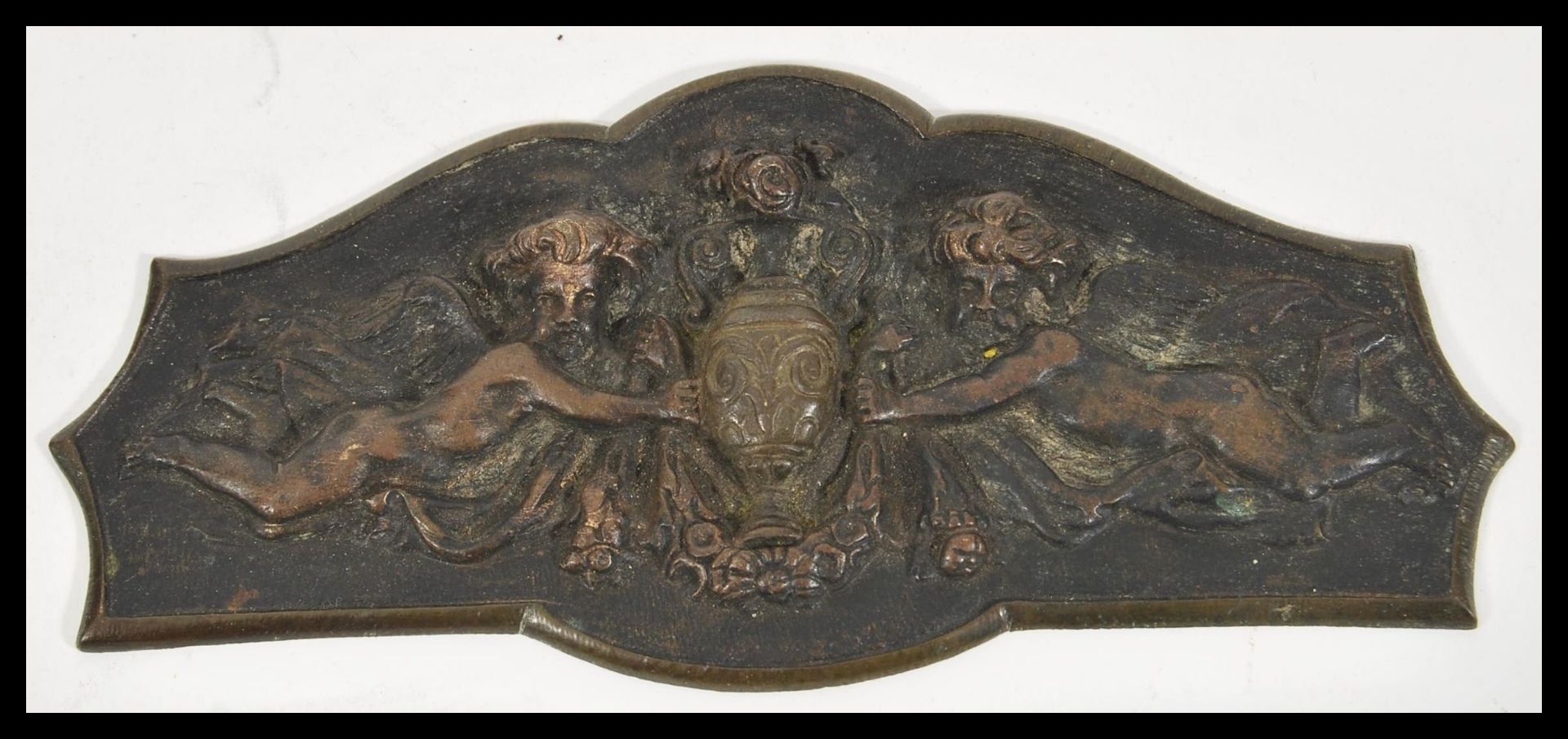 A 20th Century cast brass plaque having raised decoration of two cherubs bearing an urn and a floral