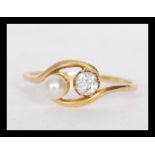 A 18ct gold ring prong set with a round cut diamond and a pearl in a cross over design. Unmarked but