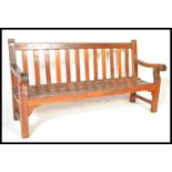 A good sized large solid teak wood garden bench of slatted form with shaped elbow rests either