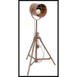 A vintage industrial floor standing adjustable spot light, raised on a metal tubular tripod frame.