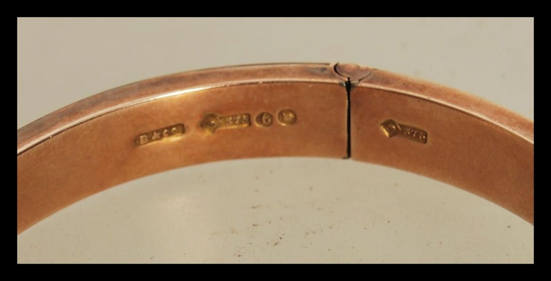 A hallmarked 9ct gold bangle having a hinged opening and safety chain. Hallmarked London 1914. - Image 3 of 4