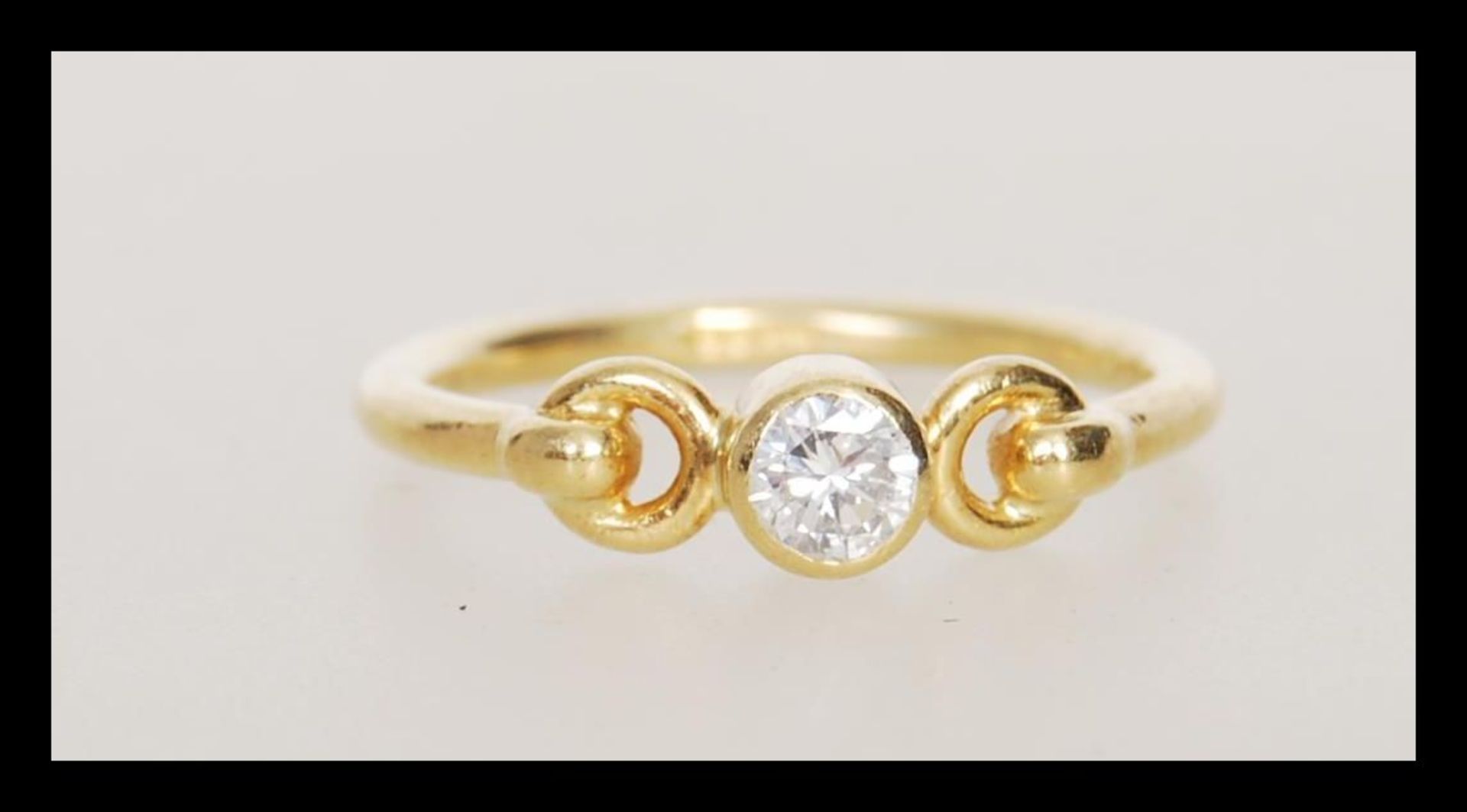 A hallmarked 18ct gold ring set bezel set with a brilliant cut diamond with decorative looped
