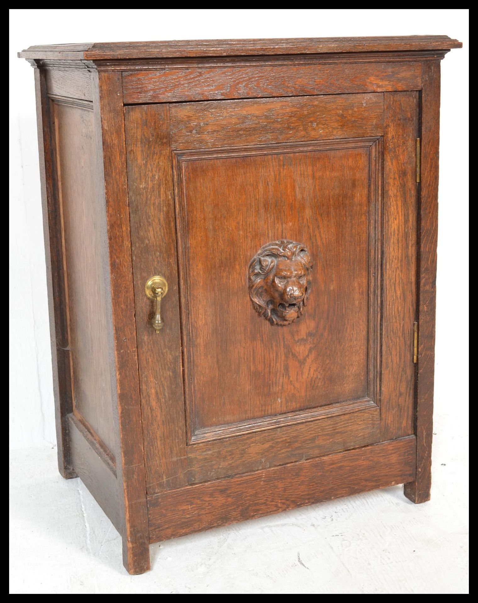 An early 20th Century unusual oak cabinet / pot cupboard having a single carved lion mask to the