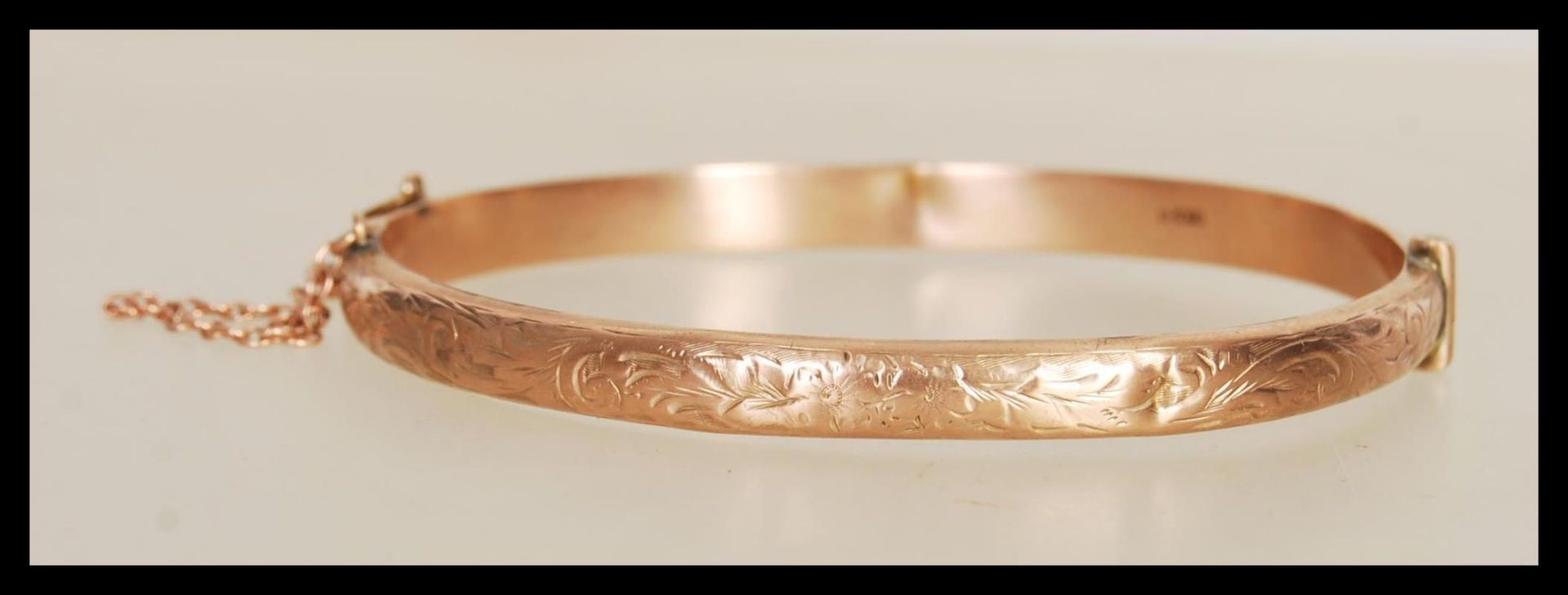 A hallmarked 9ct gold bangle bracelet with engraved floral decoration to front, having hinged