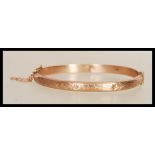 A hallmarked 9ct gold bangle bracelet with engraved floral decoration to front, having hinged