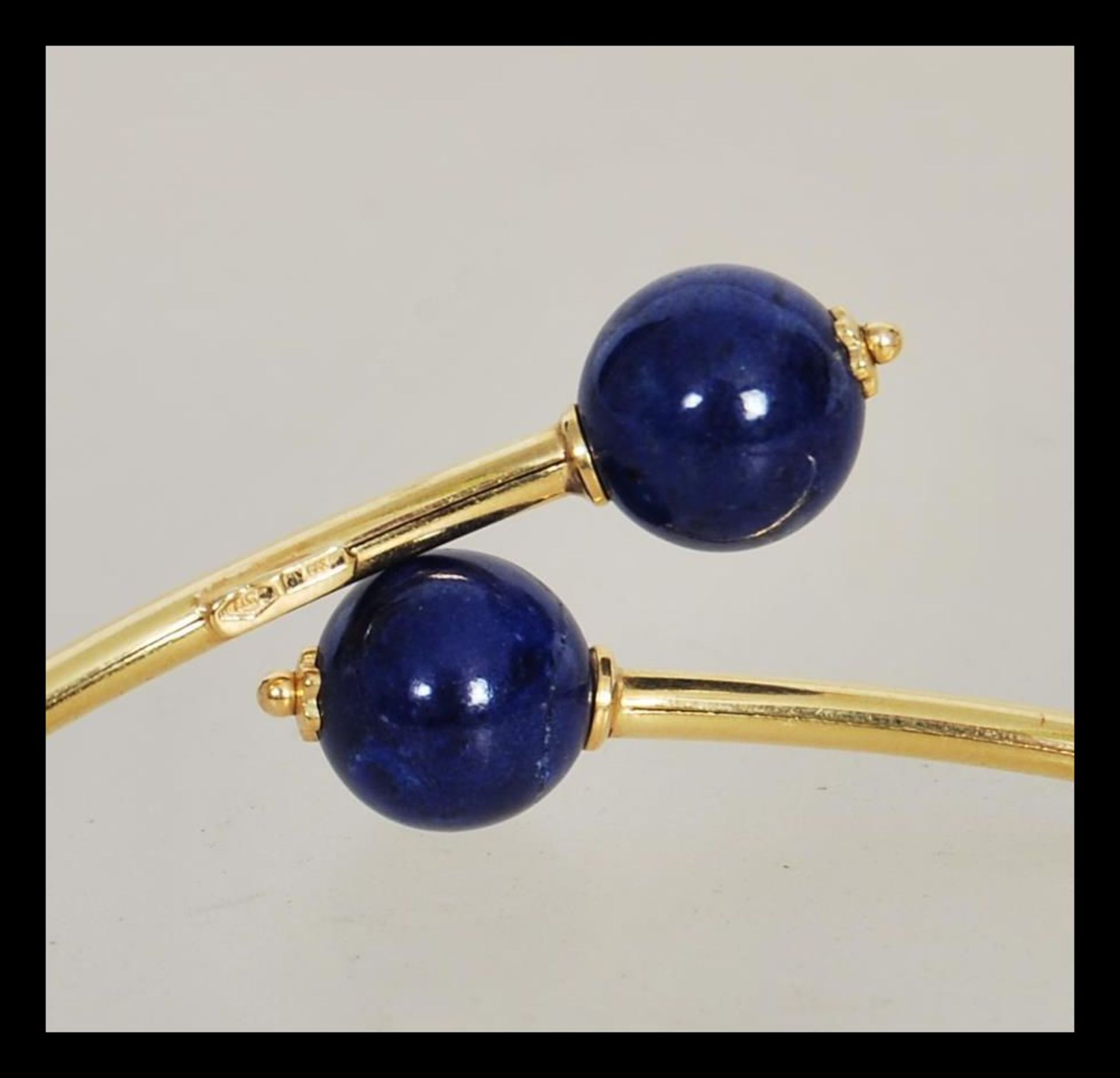 A stamped 750 18ct gold bangle bracelet finished with two blue bead stoppers. Weight 4.3g. - Image 2 of 3