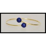 A stamped 750 18ct gold bangle bracelet finished with two blue bead stoppers. Weight 4.3g.