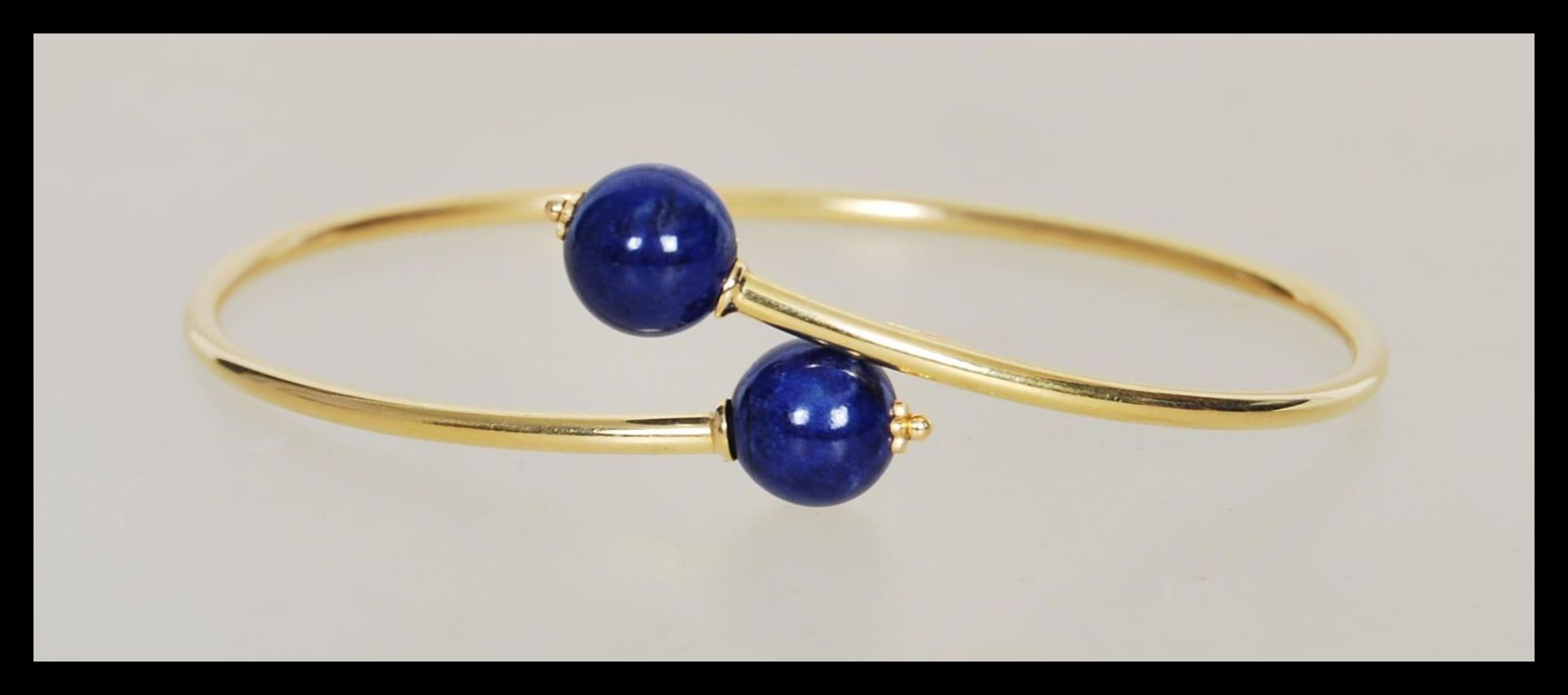 A stamped 750 18ct gold bangle bracelet finished with two blue bead stoppers. Weight 4.3g.
