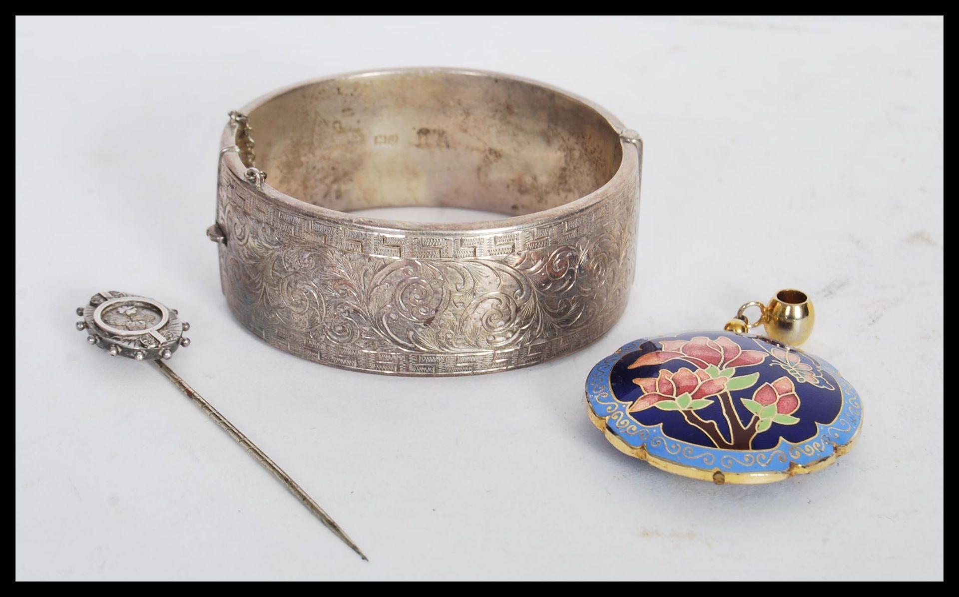 A silver hallmarked bangle bracelet having scrolled foliate and greek key engraving with a hinged