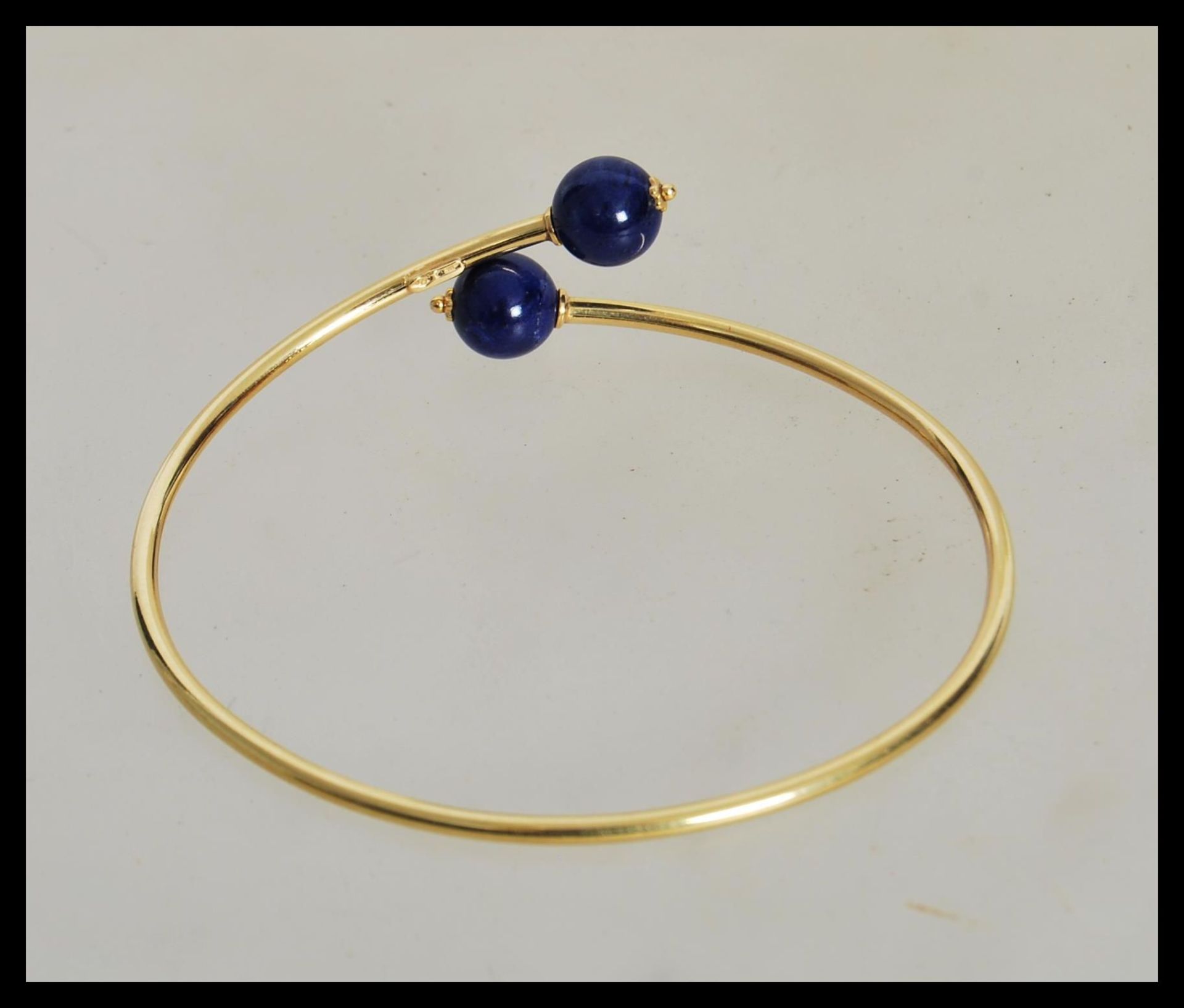 A stamped 750 18ct gold bangle bracelet finished with two blue bead stoppers. Weight 4.3g. - Image 3 of 3