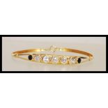 A stamped 750 18ct gold bangle bracelet set with five hexagonal cut white stones and two round cut